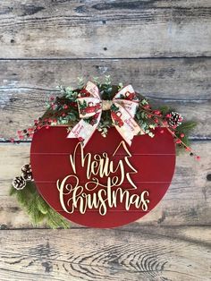 a merry christmas sign hanging on the side of a wooden wall with holly and pine cones