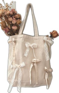 a white tote bag with flowers and ribbons on the handles, hanging from it's side