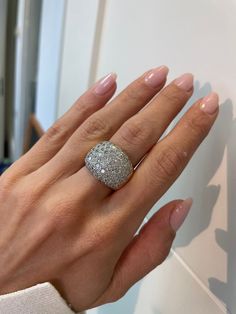 a woman's hand with a diamond ring on her left hand, against a white wall