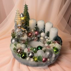 a christmas wreath with candles and ornaments in it on top of a pink table cloth