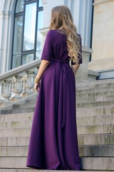 a woman in a purple dress is walking up some stairs with her back to the camera