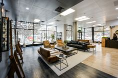 a living room filled with lots of furniture next to tall glass windows on the wall