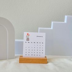 a desk calendar sitting on top of a wooden stand next to a white clock tower