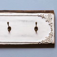 two metal hooks are attached to a white board with rope and wood trim on it