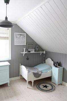 an attic bedroom with gray walls and white bedding, blue dressers and rug