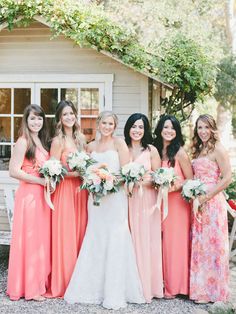 a group of women standing next to each other holding bouquets in front of a house