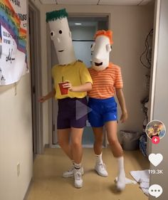 two people standing in a hallway with one person wearing a paper mask and the other holding a cup