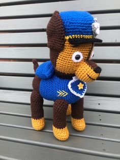 a crocheted stuffed animal is posed on a bench