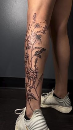 a woman's leg with flowers and leaves on it, in front of a gray wall