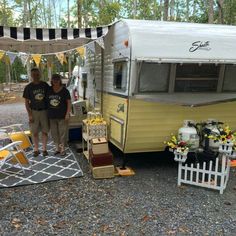 two people standing in front of a yellow and white camper parked next to each other