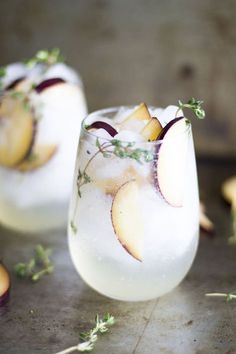 two glasses filled with ice and fruit on top of a table next to sliced apples