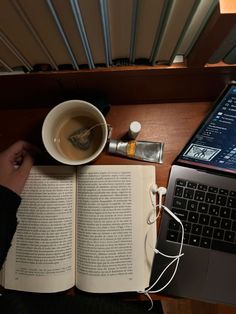 an open book sitting on top of a desk next to a laptop computer and cup of coffee