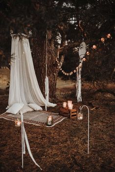 an outdoor wedding setup with candles and drapes on the ground, surrounded by trees