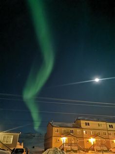 an aurora bore is seen in the night sky over a snow - covered hill and building