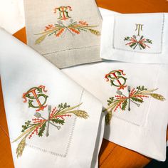 four embroidered napkins on top of an orange table cloth with monogrammed letters