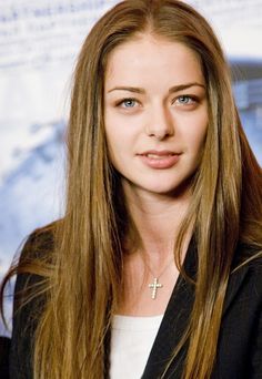 a woman with long brown hair wearing a black jacket and white shirt is looking at the camera