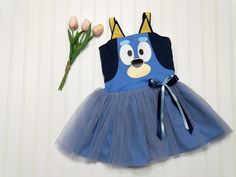 This kids Blue Heeler character dog dress is a charming and playful outfit perfect for little ones. The dress features a vibrant shade of blue, adding a pop of color to any occasion.  It has a character face and ears adorning the bodice.  The skirt has tulle over the cotton fabric adding a touch of whimsy and fun.  The back of the bodice has elastic encased for ease of dressing and will stretch for extended wear. Also available is little sister Orange Heeler. Please select Orange or Blue in the dropdown for your desired character. Sizes available are from 6 months to size 6. *Please allow two weeks from your date of order for your dress to ship.* Playful Fitted Cartoon Print Dress, Playful Cotton Dresses With Character Print, Playful Cotton Dress With Character Print, Blue Disney Dress For Costume Party, Cute Blue Cartoon Print Dress, Cute Blue Dress With Cartoon Print, Playful Blue Dress For Playtime, Playful Blue Dresses For Playtime, Fitted Fun Blue Dress