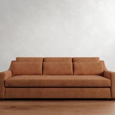 a brown couch sitting on top of a hard wood floor next to a white wall