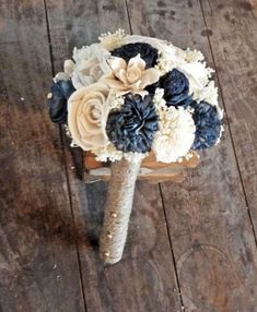 a wedding bouquet made out of flowers on top of a wooden table next to a cell phone