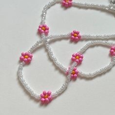 three pink and yellow flowers are attached to white beaded necklaces on a white surface