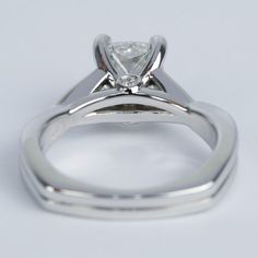 a white gold engagement ring with a princess cut diamond in the center, on a plain surface