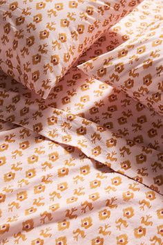 an orange and white bed spread with yellow flowers on it's side, next to a pink pillow case