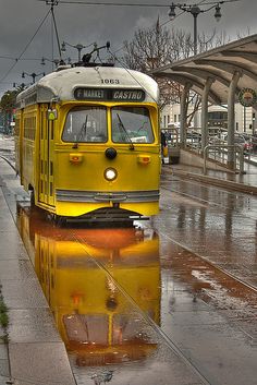 a yellow trolley car is parked on the side of the road as it rains down