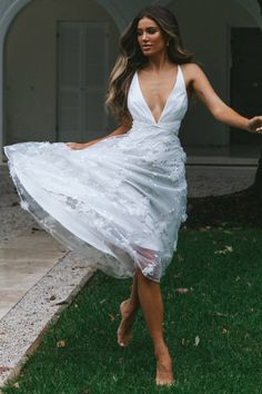 a woman in a white dress is walking on the grass