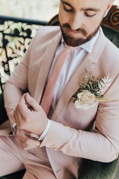 a man in a pink suit and flower boutonniere looks down at his watch