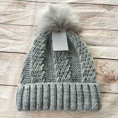 a gray knit hat with a pom - pom on the top and a white tag attached to it