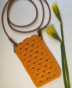 an orange crocheted purse sitting next to a yellow flower