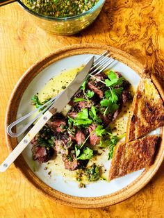 a white plate topped with meat and greens next to a bowl of mustard, bread