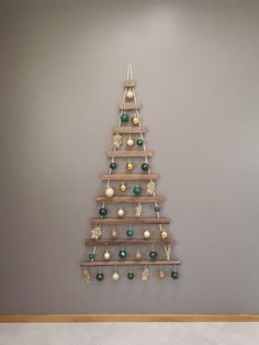 a wooden christmas tree with ornaments hanging from it's sides on a wall in an empty room