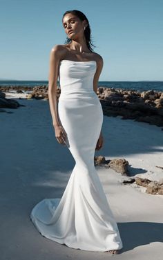 a woman standing on top of a sandy beach wearing a white dress and heels with her hands in her pockets