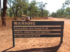 a sign warning about crocodiles and alligators in the national park on a dirt road