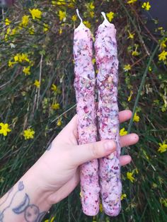 someone holding two candles in front of some flowers