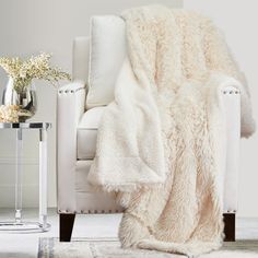 a white chair with a blanket on top of it next to a vase filled with flowers