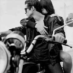 a man riding on the back of a motorcycle next to a woman with her arm around him