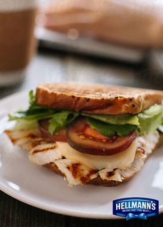 a grilled chicken sandwich with lettuce, tomato and cheese on a white plate