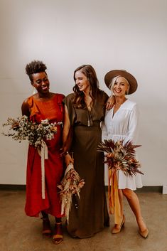 three women standing next to each other in dresses and hats with flowers on their heads