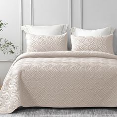 a bed with white sheets and pillows in a room next to a potted plant