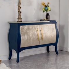 a blue and gold cabinet with flowers on top in a white walled room next to a door