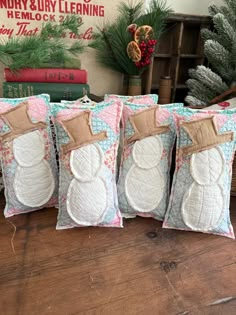 four snowman pillows sitting on top of a wooden table next to christmas tree branches