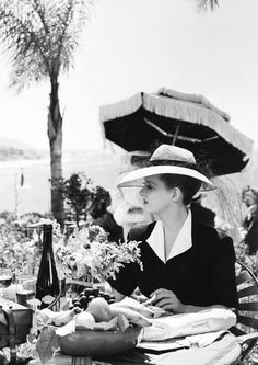 a black and white photo of a woman sitting at a table with an umbrella over her head