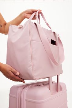 a woman is holding a pink bag on top of a piece of luggage with her hand