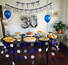 a table topped with lots of food next to blue and white balloons in the shape of 30