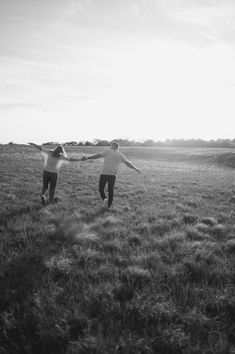 two people are running in the grass holding hands