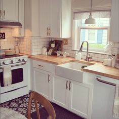 a kitchen with white cabinets and wood counter tops, an oven, dishwasher and sink