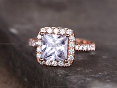 an engagement ring with a square cut diamond surrounded by smaller round diamonds on a rock