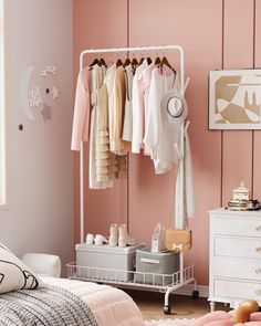 a bedroom with pink walls and clothes hanging on the rack in front of a bed